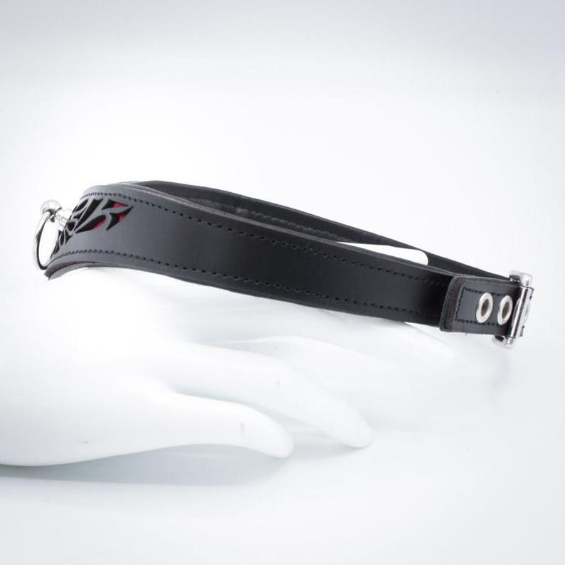 May include: Black leather collar with a red cutout design and silver hardware. The collar has two silver rings and a silver buckle.