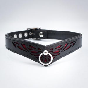 May include: Black leather collar with a red velvet lining and a silver metal ring. The collar features a cut-out design in the shape of a butterfly.