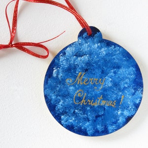 May include: Blue and white Christmas ornament with a red ribbon and the words "Merry Christmas!" written in gold.