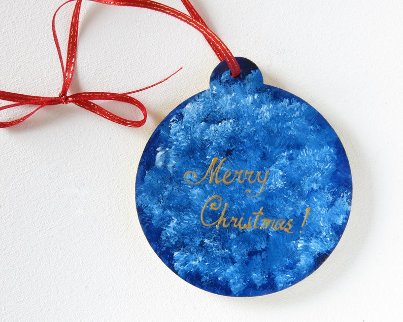 May include: Blue and white Christmas ornament with a red ribbon and the words "Merry Christmas!" written in gold.