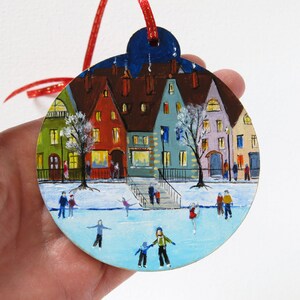 May include: Hand-painted wooden ornament depicting a winter scene with colorful houses, a frozen lake, and people ice skating. The ornament is decorated with a red ribbon.