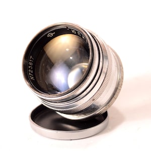 May include: A silver camera lens with a black rim and a clear glass element. The lens has the number "N723817" printed on the side.