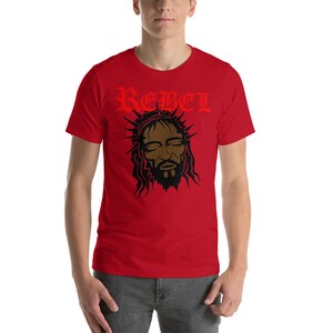 May include: Red short-sleeved t-shirt with a black and brown illustration of a person with a crown of thorns and the word "REBEL" in red lettering.
