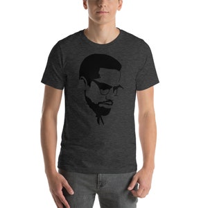 May include: A dark heather grey t-shirt with a black silhouette of Malcolm X wearing glasses.