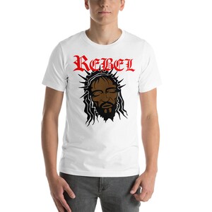 May include: White t-shirt with a black and brown image of a man's face with a crown of thorns and the word "REBEL" in red letters above the image.