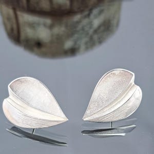 May include: A pair of silver leaf-shaped earrings with a textured surface.