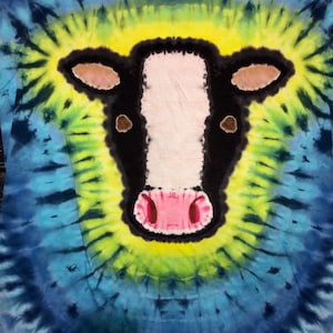 May include: A tie-dye t-shirt with a black and white cow face design. The cow's nose is pink and the background is a blue and green swirl.