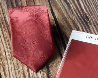 Può includere: Cravatta paisley color cannella con un motivo dettagliato. Accanto, una cartella colori "Cinnamon" di David's Bridal. La cravatta, in tessuto lucido, è appoggiata su una superficie di legno.