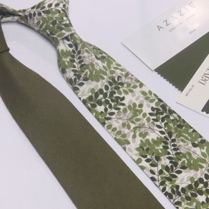 Puede incluir: Dos corbatas verdes, una lisa y otra con fondo blanco y un patrón de hojas verdes. La corbata estampada está etiquetada como "AZAZIE CHIFFON LINING Olive". La corbata lisa está etiquetada como "DAVIDS BRIDAL  MATTE OLIVE  GREEN"