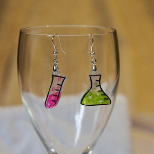 May include: A pair of earrings featuring a pink test tube and a green flask, both with silver hooks.