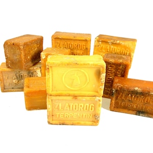 May include: A stack of yellow bar soaps with the text "Zlatorog Terpentin" printed on them. The soaps are arranged in a pile on a white surface.