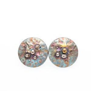 May include: A pair of round, blue and gold earrings with a textured surface and small metallic accents.