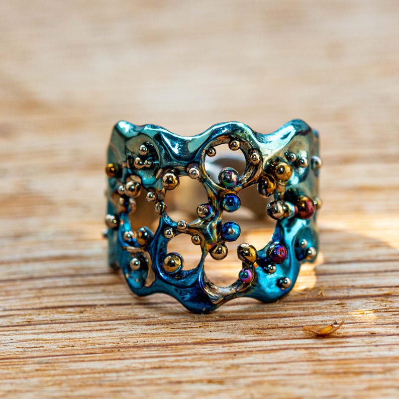 May include: A blue and gold ring with a textured, organic design. The ring is made of metal and has a unique, abstract shape.