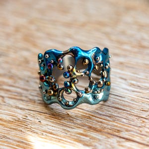 May include: A blue and silver ring with a unique, organic design. The ring is made of metal and has a textured surface. The ring is decorated with small, colorful beads.