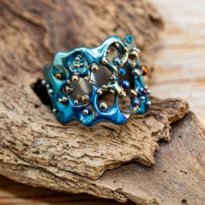 May include: A blue and silver ring with a textured, organic design. The ring is made of metal and has a unique, abstract look.