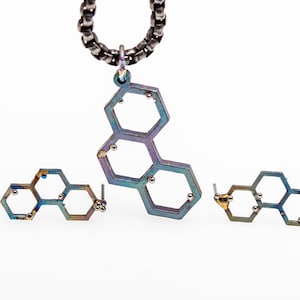 Op de afbeelding: Een set met iriserende blauwe en gouden sieraden met een hanger en oorbellen. De hanger en oorbellen zijn gemaakt van meerdere verbonden zeshoekige vormen met kleine gouden kralen in het midden van elke zeshoek.