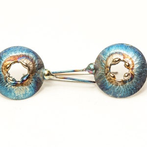 May include: A pair of blue and gold earrings with a circular design and a small hole in the center. The earrings have a textured surface and a metallic finish.