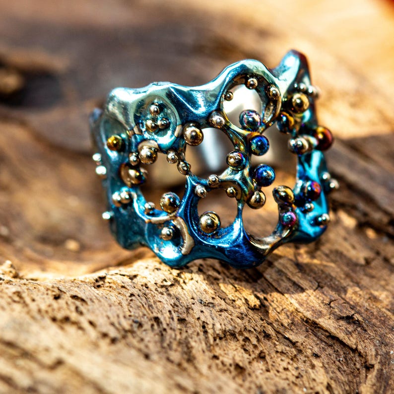 May include: A blue and gold ring with a unique, organic design. The ring is made of metal and has a textured surface. The ring is set with small, round beads.