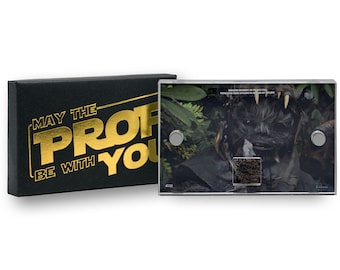 May include: A clear acrylic frame with a black background and a close-up of a creature from the Star Wars movie franchise. The creature has a dark brown fur and a toothy grin. The frame has a gold inscription that reads "May the Force be with you".