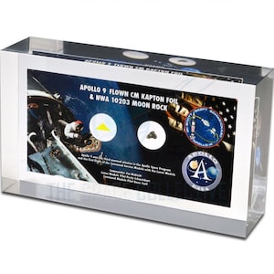 Può includere: Un blocco di acrilico trasparente con un'immagine stampata di un astronauta in tuta spaziale, un piccolo pezzo di roccia lunare e un pezzo di foglio di Kapton. Il testo sull'immagine recita "Apollo 9 Flown CM Kapton Foil & NWA 10203 Moon Rock".