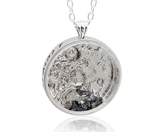 May include: A silver necklace with a round pendant featuring a textured, silver surface with a dark gray center. The pendant is attached to a silver chain.