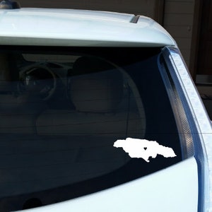 May include: A white car with a white outline of Jamaica with a heart in the middle on the back window.
