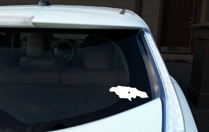 May include: A white car with a white outline of Jamaica with a heart in the middle on the back window.