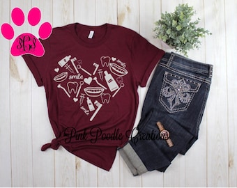 May include: A maroon t-shirt with a white heart design featuring dental tools, teeth, and the word "smile".