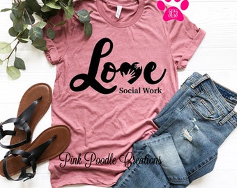 May include: A pink t-shirt with the words "Love Social Work" in black lettering. The word "Love" has a heart shape with hands inside it.