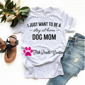 Puede incluir: Una camiseta gris con el texto "I JUST WANT TO BE A - stay at home - DOG MOM" en negro. Una huella de pata rosa con el texto "Pink Poodle Creations" est&aacute; debajo del texto.
