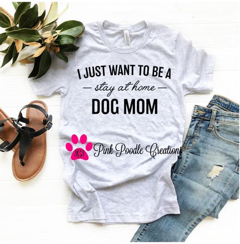 Puede incluir: Una camiseta gris con el texto "I JUST WANT TO BE A - stay at home - DOG MOM" en negro. Una huella de pata rosa con el texto "Pink Poodle Creations" est&aacute; debajo del texto.