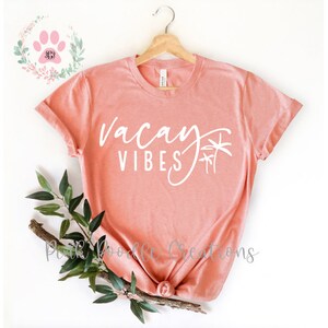 May include: A peach-colored t-shirt with the text "vacay vibes" and palm trees in white.