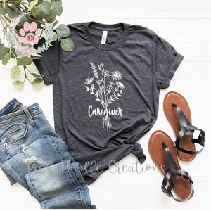 May include: A dark gray t-shirt with a white floral design and the word "Caregiver" printed on the front.