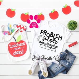 May include: White t-shirt with the text "PROBLEM solver #mathtteacher" in black. A red pencil and ruler are drawn next to the text. A white tote bag with a red apple and the text "teachers have class!" is in the image.