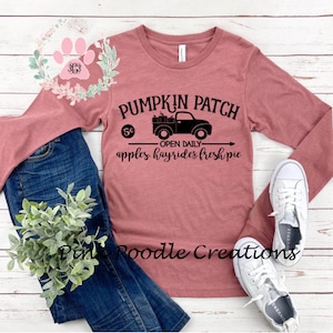 May include: A long-sleeved, mauve t-shirt with a black graphic design of a pickup truck with pumpkins in the bed. The text "Pumpkin Patch" is above the truck, and "5¢ - Open Daily - apples hayrides fresh pie" is below the truck.