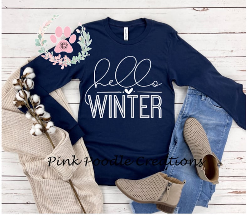 May include: Navy blue long-sleeve shirt with the words "hello WINTER" in white script. The shirt is paired with blue jeans, tan booties, and a beige cardigan. A sprig of cotton and a floral design are also in the image.