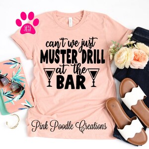 May include: A peach-colored t-shirt with the text "can't we just muster drill at the bar" in black lettering with two martini glass graphics. The text "Pink Poodle Creations" is printed in black at the bottom of the shirt.
