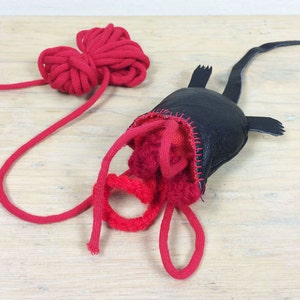 May include: A black leather creature with red stitching and a long neck, with red yarn spilling out. A ball of red yarn is also present. The craft item is likely a toy or decorative piece.