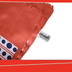 Pode incluir: Um len&ccedil;o de seda cor coral com um padr&atilde;o de bolinhas e listras brancas e azul marinho. O len&ccedil;o tem uma borda com franjas e uma etiqueta que diz "Diolen made in Europe."