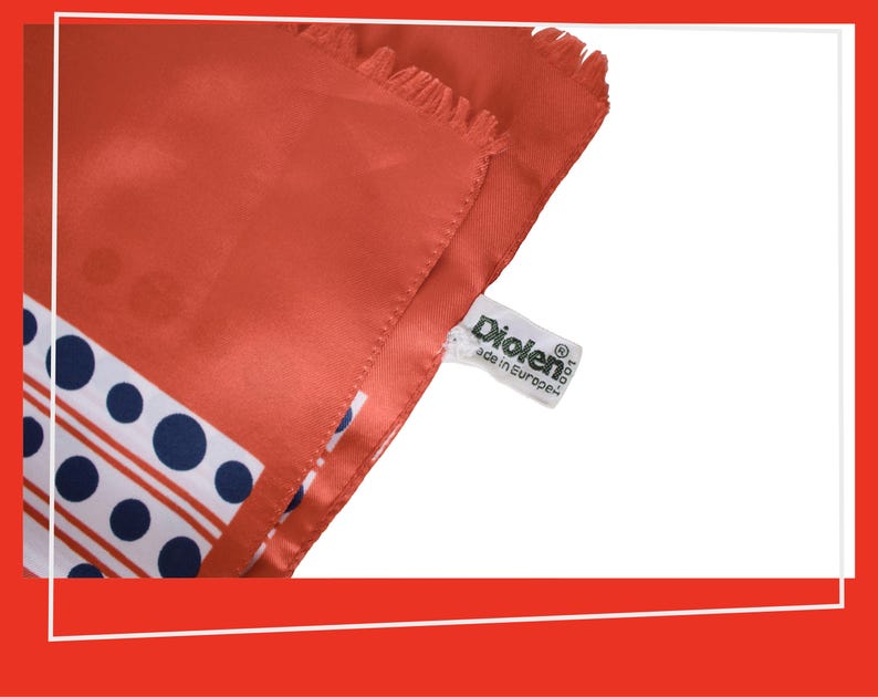 Pode incluir: Um len&ccedil;o de seda cor coral com um padr&atilde;o de bolinhas e listras brancas e azul marinho. O len&ccedil;o tem uma borda com franjas e uma etiqueta que diz "Diolen made in Europe."