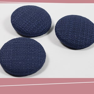 May include: Three dark blue fabric covered buttons. The buttons are round and have a textured surface.