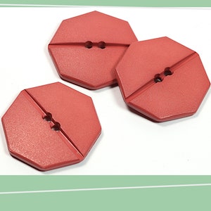 May include: Three red octagonal buttons with two holes each. The buttons have a matte finish and a slightly textured surface.