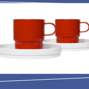 May include: Two red mugs with handles sit on white saucers. The mugs have a cylindrical shape and are stacked on a base. The saucers are round with a slightly raised edge. The background is white.