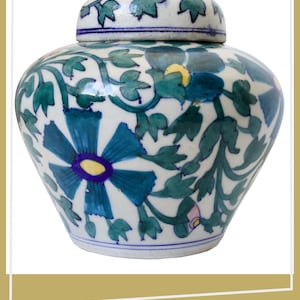 Op de afbeelding: Een keramieken gemberpot met deksel, voorzien van een witte basis versierd met handgeschilderde blauwe en groene bloemmotieven, waaronder grote blauwe bloemblaadjes met gele harten en groene bladranken rondom de ronde buik.