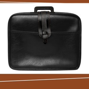 Peut inclure: Une valise en cuir noir avec une poignée en cuir marron et une sangle en cuir marron.