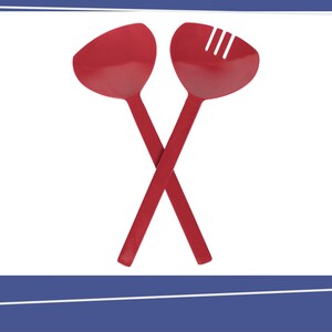 May include: A pair of red salad servers consisting of a solid spoon and a slotted spoon with three vertical cutouts. The two utensils are positioned in a crossed "X" formation against a plain white background, featuring long handles.
