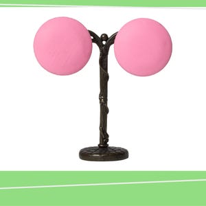 May include: A decorative bronze-colored metal stand featuring two large, round, pink objects. The stand has a detailed, textured base and a central stem with a branch-like design, creating a unique and artistic display.