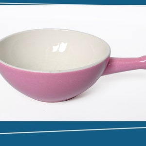 Op de afbeelding: Een roze keramische kom met een witte binnenkant en een handvat. De kom is ontworpen om kleine porties voedsel te serveren.
