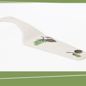 May include: White ceramic cake server with a pine needle and pine cone design.