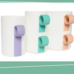 Op de afbeelding: Set van vier witte keramische mokken met kleurrijke handvatten. De mokken hebben een enkele gekleurde streep aan de zijkant. De handvatten zijn in pastelroze, paars, groen en blauw.